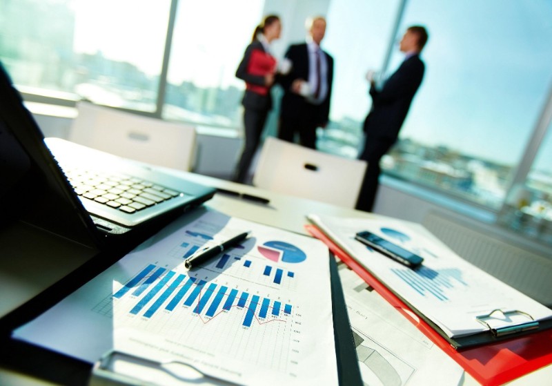 papers with charts and assessments of customer behavior are on the desk next to a laptop