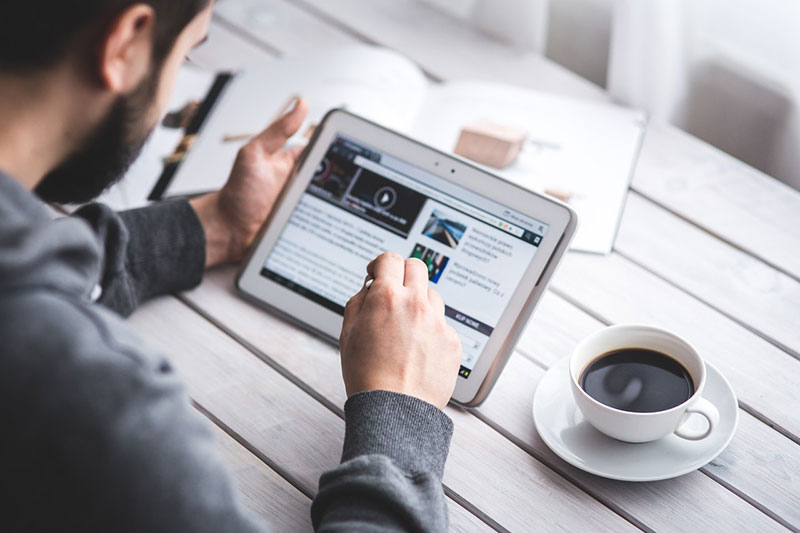 a person working on a smart device, with a cup of coffee next to them